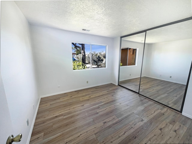 unfurnished bedroom featuring a closet, baseboards, a textured ceiling, and wood finished floors