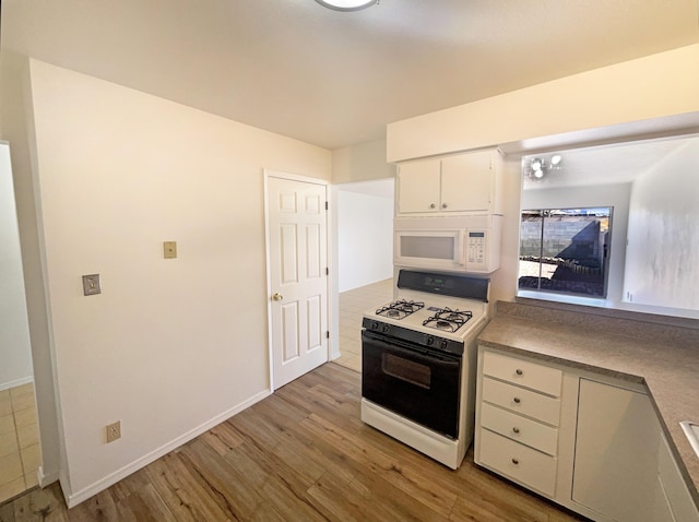 kitchen with range with gas stovetop, white microwave, baseboards, white cabinets, and light wood-type flooring