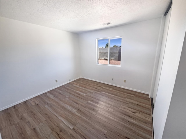 spare room with visible vents, a textured ceiling, baseboards, and wood finished floors