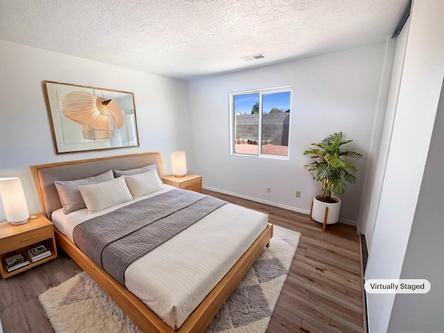 bedroom featuring visible vents, a textured ceiling, baseboards, and wood finished floors