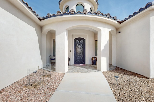 view of exterior entry with a tiled roof and stucco siding