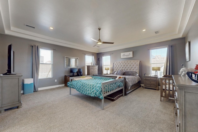 bedroom with a tray ceiling, visible vents, multiple windows, and light colored carpet