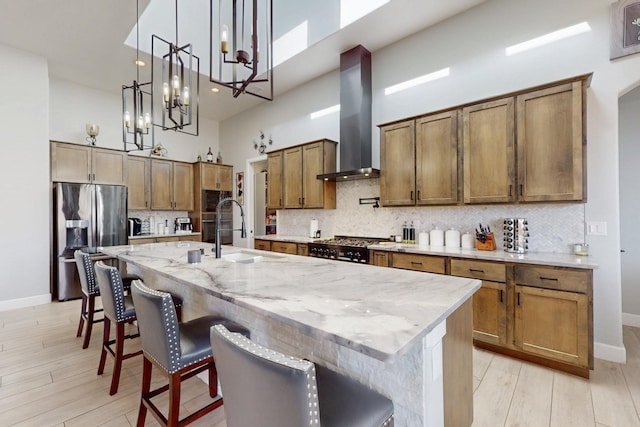 kitchen with a sink, a high ceiling, wall chimney range hood, and stainless steel fridge with ice dispenser