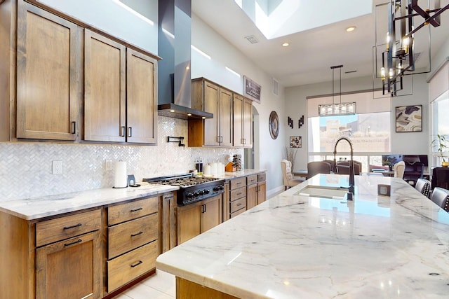 kitchen with a sink, light stone counters, wall chimney exhaust hood, and stainless steel gas cooktop