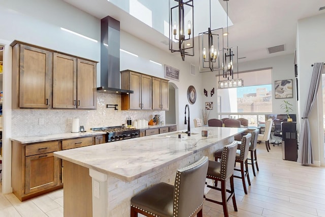 kitchen with visible vents, arched walkways, a sink, wall chimney range hood, and backsplash