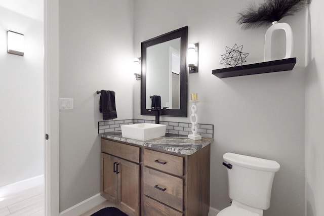 half bath with vanity, toilet, baseboards, and backsplash