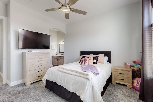 bedroom with baseboards, ceiling fan, light colored carpet, ensuite bathroom, and arched walkways