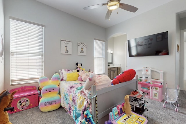 carpeted bedroom featuring arched walkways, a ceiling fan, and ensuite bathroom