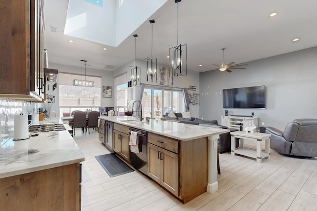 kitchen featuring light stone countertops, open floor plan, black dishwasher, a ceiling fan, and a sink