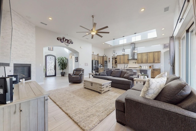 living area featuring a fireplace, a high ceiling, a ceiling fan, and visible vents