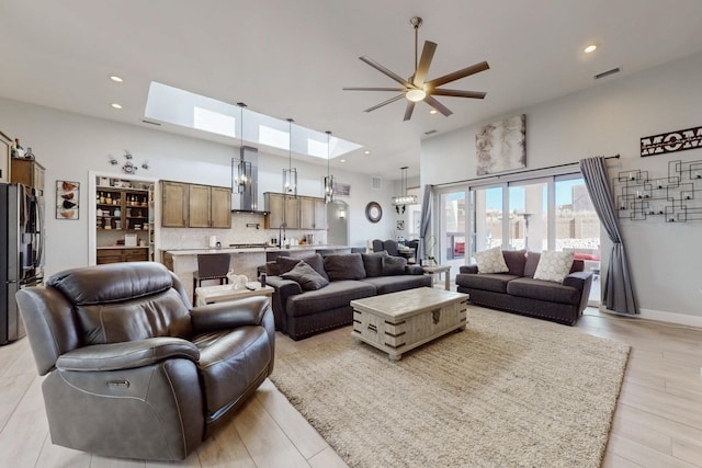 living room featuring light wood finished floors, visible vents, ceiling fan, a skylight, and a towering ceiling