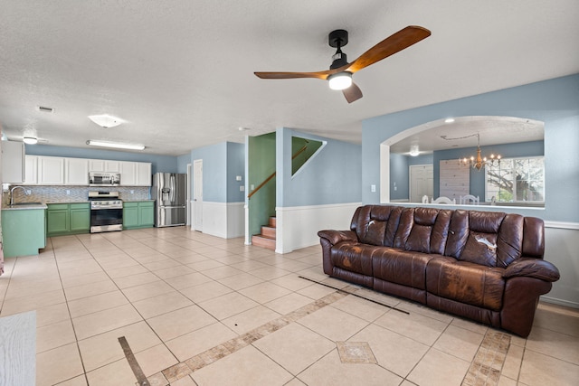 living room featuring stairway, light tile patterned floors, arched walkways, a textured ceiling, and ceiling fan with notable chandelier