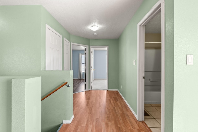 hall with an upstairs landing, light wood-style floors, baseboards, and a textured ceiling