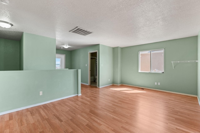 empty room featuring visible vents, plenty of natural light, baseboards, and wood finished floors