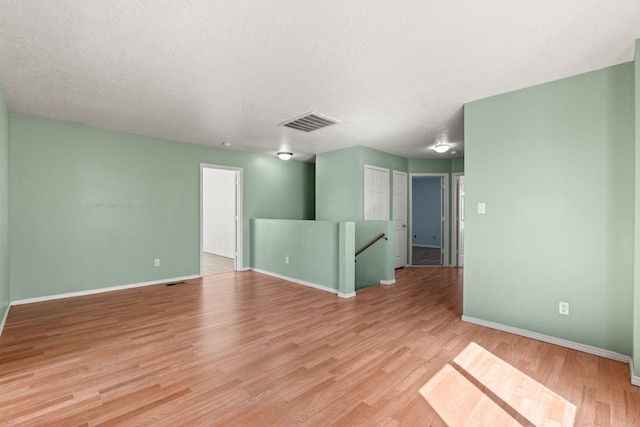 empty room with visible vents, baseboards, light wood-style floors, and a textured ceiling