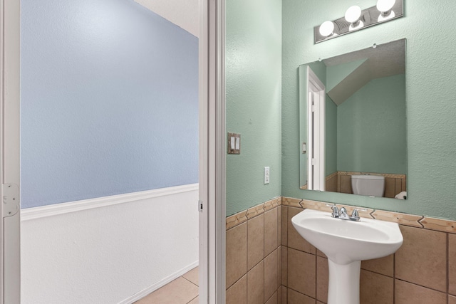 half bath with tile patterned flooring, wainscoting, toilet, and tile walls