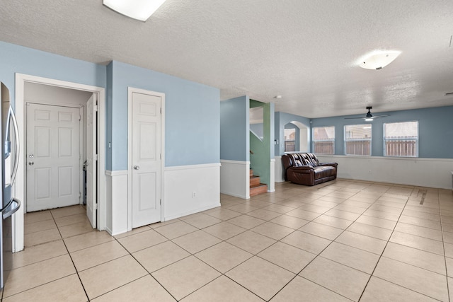 unfurnished living room with light tile patterned floors, arched walkways, ceiling fan, stairs, and a textured ceiling