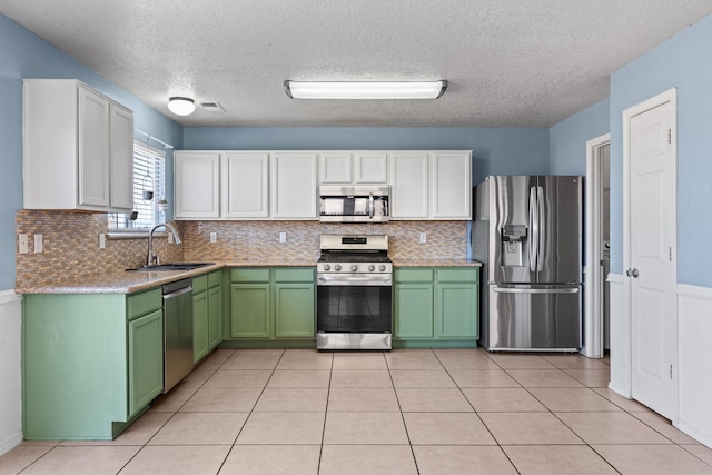 kitchen with green cabinetry, light tile patterned floors, appliances with stainless steel finishes, white cabinets, and a sink