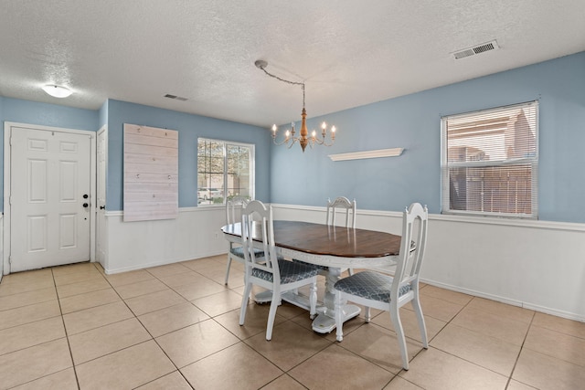 dining space with light tile patterned floors, visible vents, a textured ceiling, and an inviting chandelier