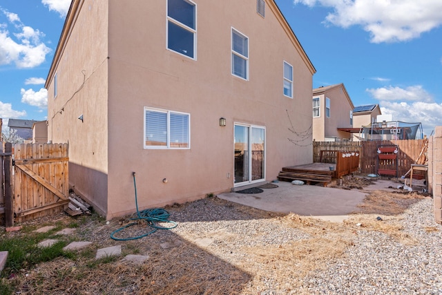 rear view of property with stucco siding, a patio, a deck, and fence