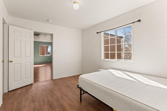 bedroom with multiple windows, a textured ceiling, baseboards, and wood finished floors