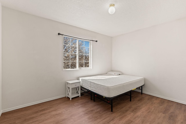 bedroom featuring wood finished floors, baseboards, and a textured ceiling