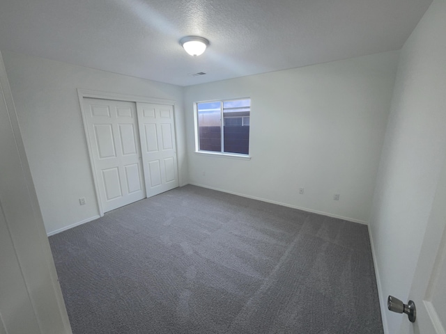 unfurnished bedroom with visible vents, baseboards, a closet, a textured ceiling, and dark colored carpet