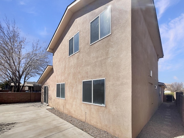 view of side of home with a patio, fence, and stucco siding