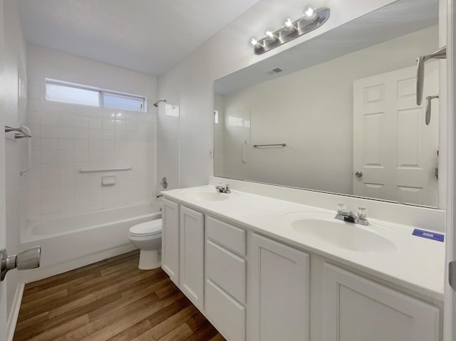 full bath with double vanity, toilet, wood finished floors, and a sink