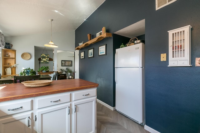 kitchen featuring decorative light fixtures, wood counters, white cabinetry, freestanding refrigerator, and vaulted ceiling