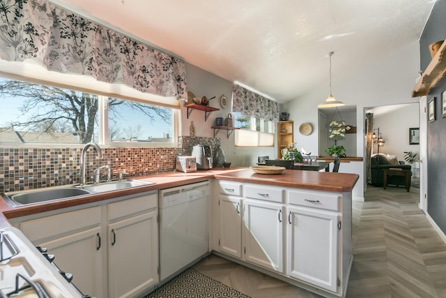 kitchen featuring white cabinetry, lofted ceiling, a peninsula, a sink, and dishwasher