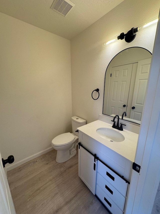 half bathroom featuring visible vents, toilet, a textured ceiling, wood finished floors, and vanity