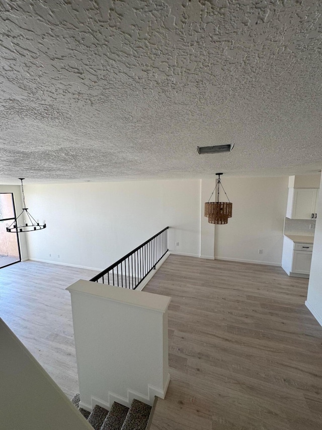 stairway with baseboards, a textured ceiling, an inviting chandelier, and wood finished floors