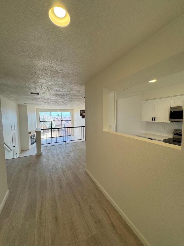 corridor with a notable chandelier, wood finished floors, baseboards, and a textured ceiling