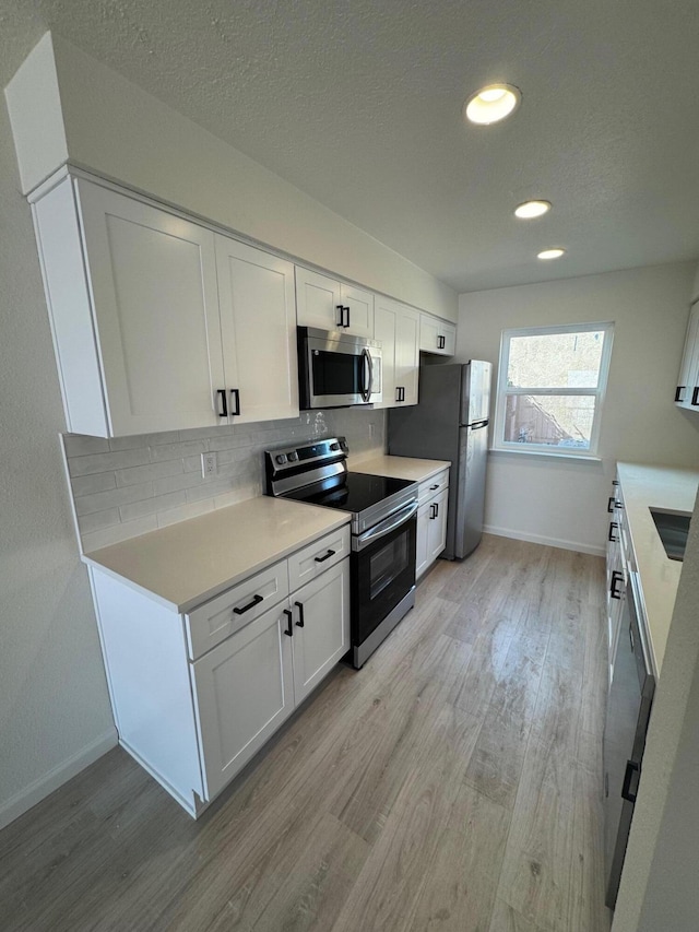 kitchen with light wood-style floors, appliances with stainless steel finishes, light countertops, and white cabinetry