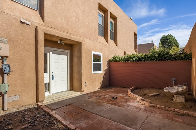 entrance to property featuring stucco siding, a patio, and fence