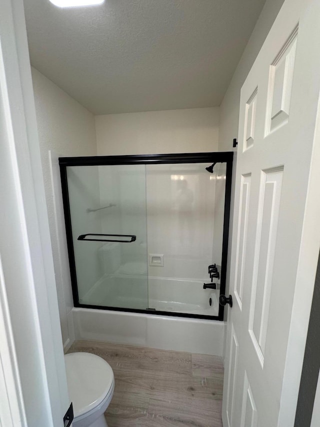 bathroom with toilet, wood finished floors, shower / bath combination with glass door, and a textured ceiling