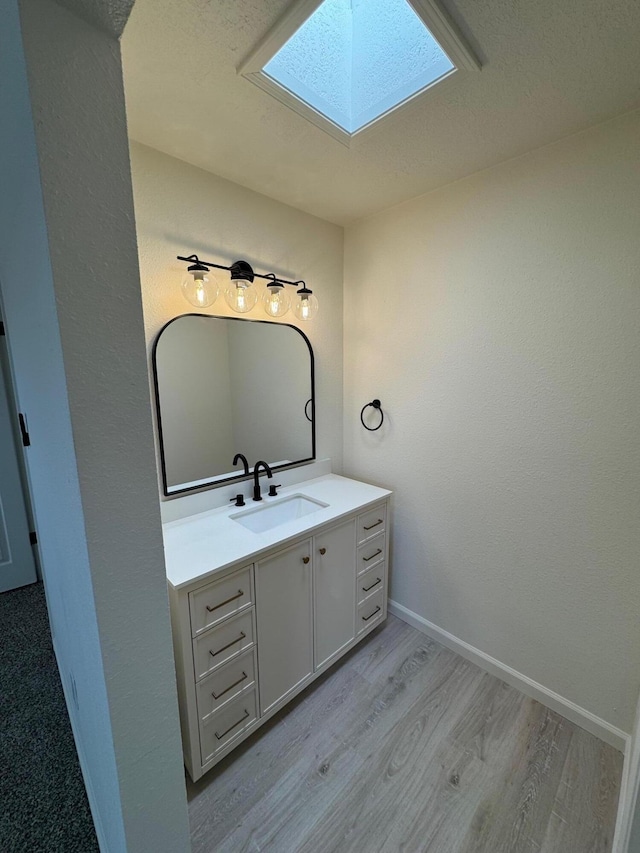 bathroom featuring baseboards, wood finished floors, a skylight, and vanity