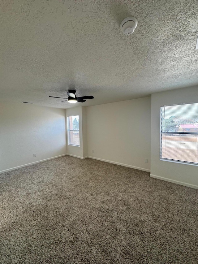 empty room featuring carpet flooring, a textured ceiling, a ceiling fan, and baseboards