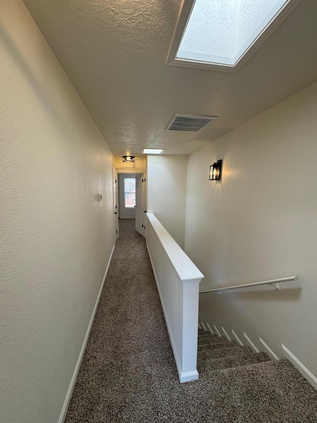 hall with baseboards, visible vents, a textured ceiling, carpet flooring, and an upstairs landing