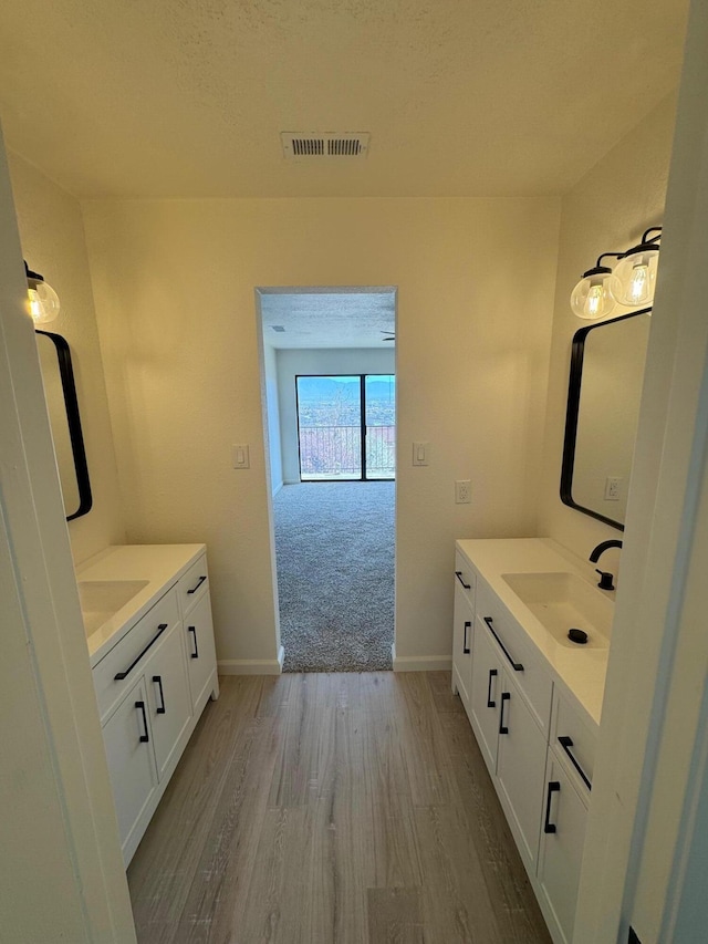 bathroom featuring visible vents, wood finished floors, two vanities, and a sink