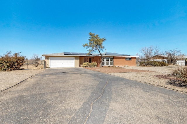 ranch-style home with a garage, fence, solar panels, and aphalt driveway