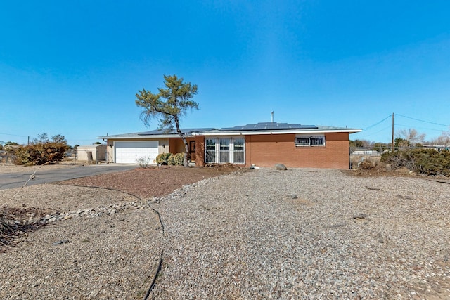 view of front of property featuring fence, solar panels, an attached garage, concrete driveway, and brick siding