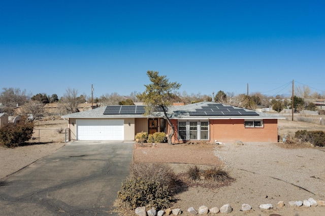 ranch-style home with a garage, roof mounted solar panels, driveway, and fence