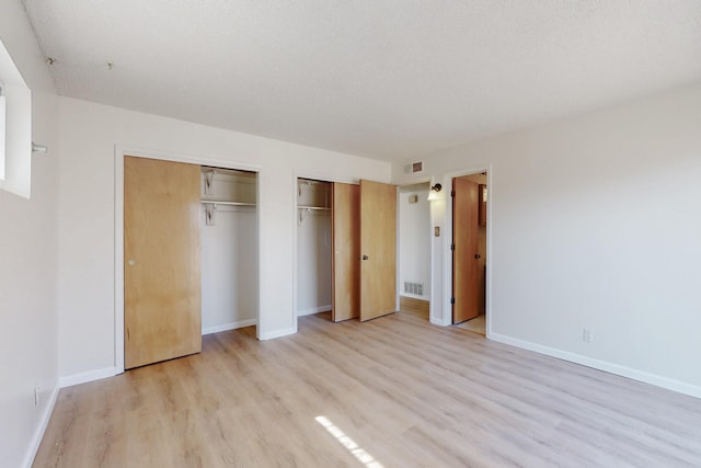 unfurnished bedroom featuring light wood finished floors, visible vents, baseboards, and multiple closets