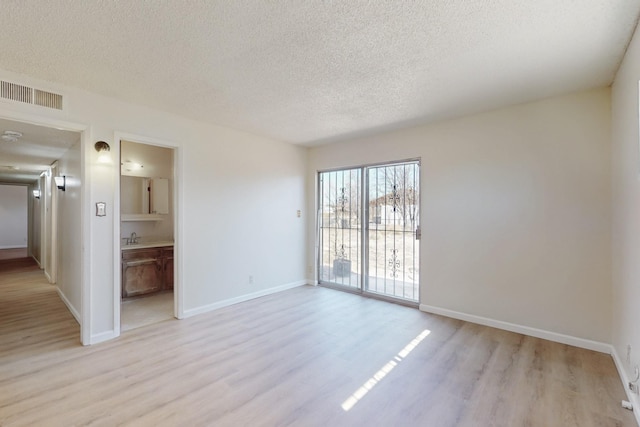 unfurnished room featuring baseboards, visible vents, light wood finished floors, and a textured ceiling