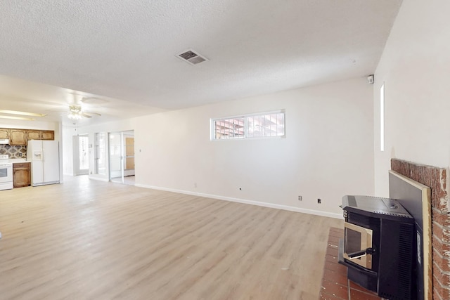 living room with visible vents, baseboards, light wood-type flooring, a wood stove, and a ceiling fan