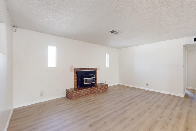 unfurnished living room with visible vents, light wood-style flooring, a textured ceiling, baseboards, and a wood stove