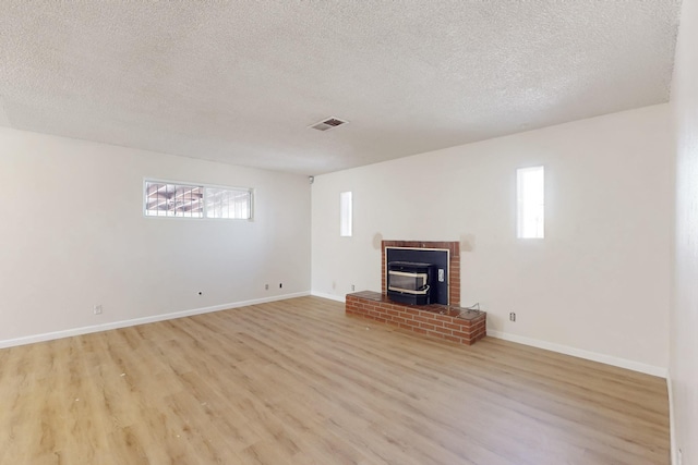 unfurnished living room featuring a wood stove, baseboards, visible vents, and light wood finished floors