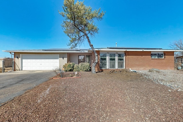 ranch-style home featuring brick siding, roof mounted solar panels, an attached garage, and driveway